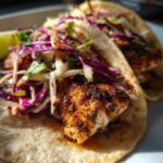 Close-up of two Air Fryer Fish Tacos filled with seasoned fish, red cabbage slaw, and cilantro, with a lime wedge.