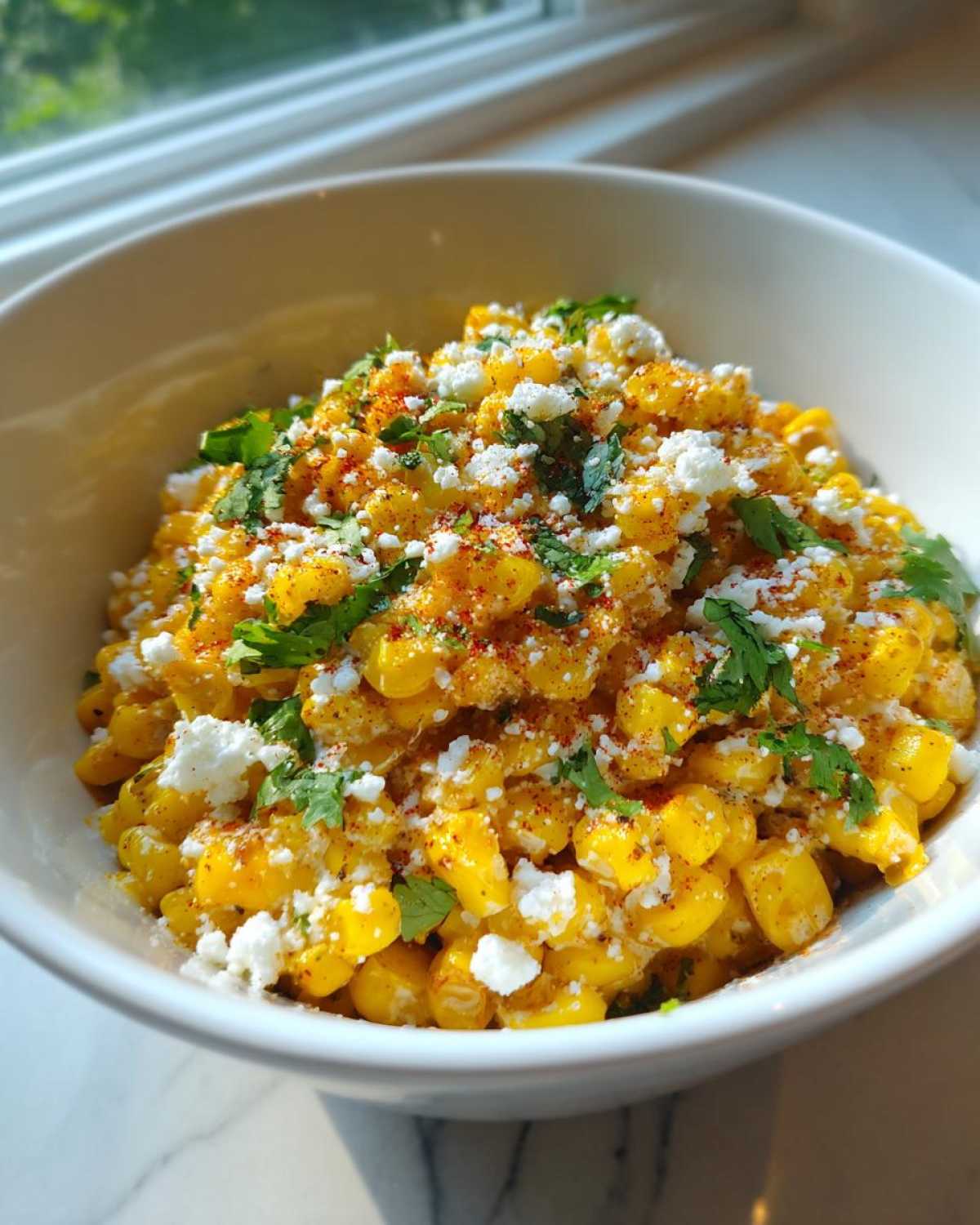 Close-up of air fryer Mexican street corn in a white bowl, topped with crumbled cotija cheese, cilantro, and chili powder.