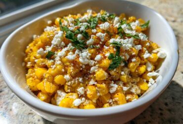 A white bowl filled with vibrant yellow air fryer Mexican street corn, topped with crumbled white cheese and fresh cilantro.