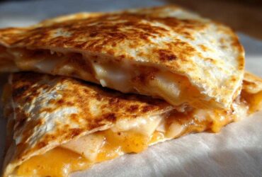 Close-up of two halves of a golden-brown Apple Cheddar Quesadilla, revealing melted cheddar cheese and apple filling.