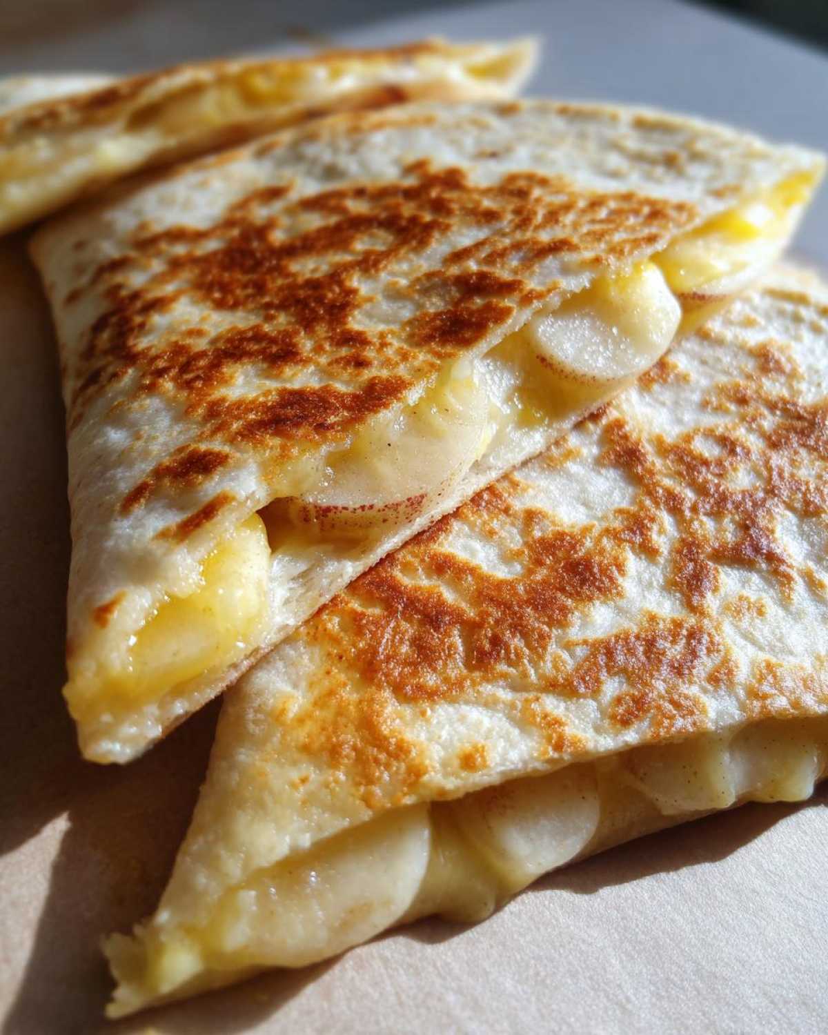 Close-up of golden-brown Apple Cheddar Quesadillas, sliced into triangles, with melted cheese and apple slices visible.