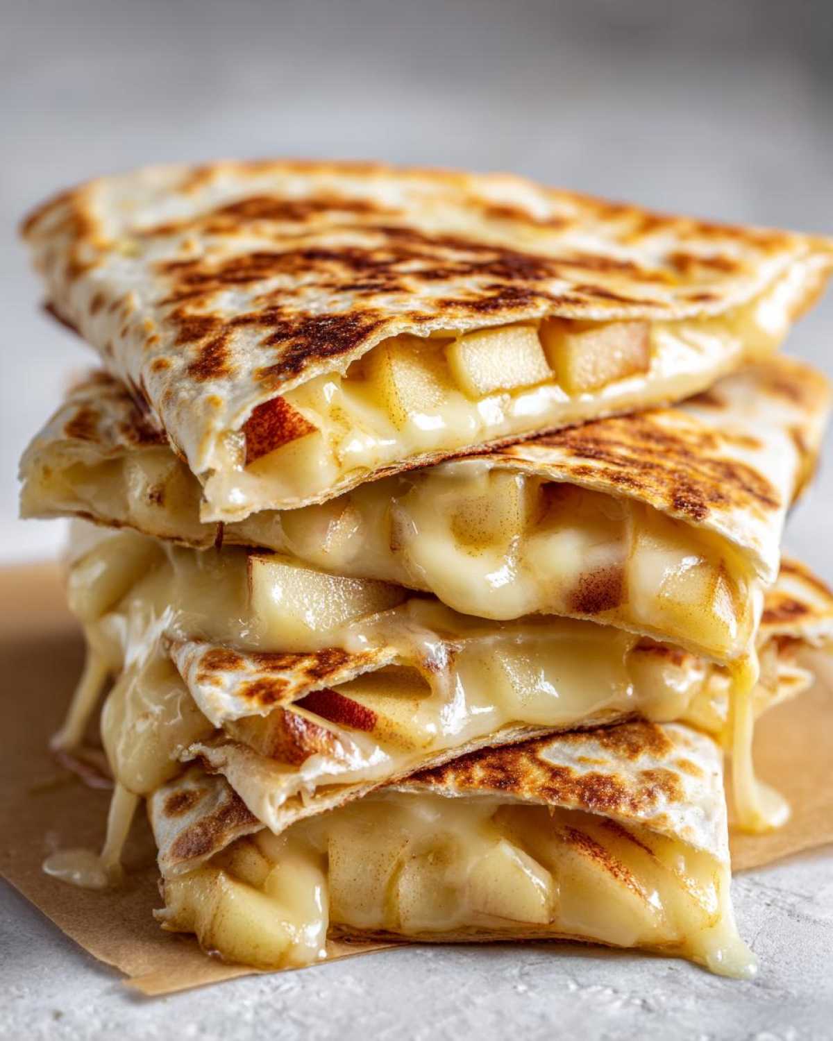 A stack of golden-brown Apple Cheddar Quesadillas, oozing with melted cheese and filled with diced apples.