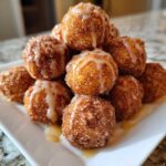 A stack of freshly made Apple Cider Donut Holes coated in cinnamon sugar and drizzled with a sweet glaze.