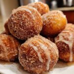 A close-up of a pile of freshly made Apple Cider Donut Holes, coated in cinnamon sugar and drizzled with a sweet glaze.