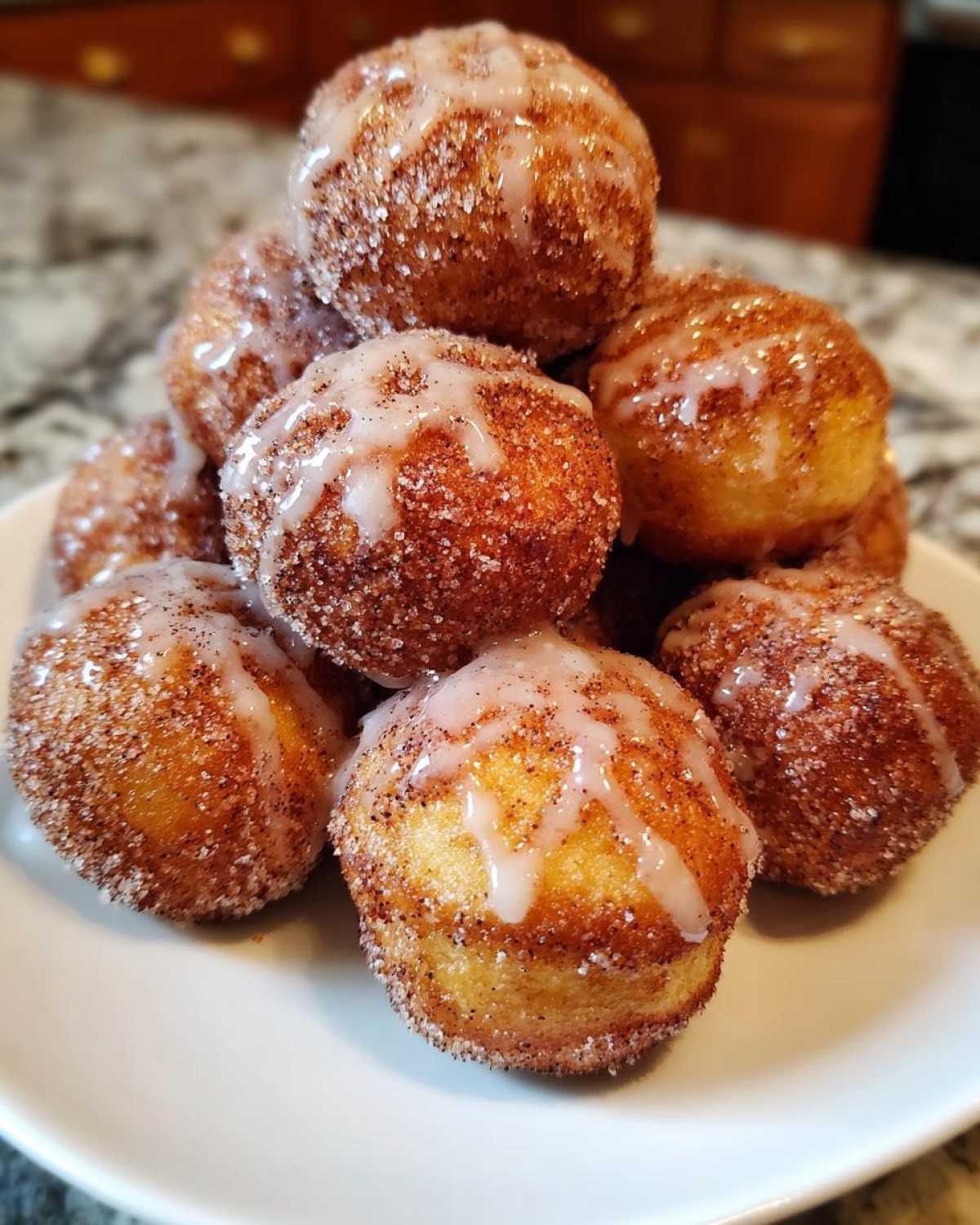 A stack of freshly baked Apple Cider Donut Holes coated in cinnamon sugar and drizzled with a sweet glaze.