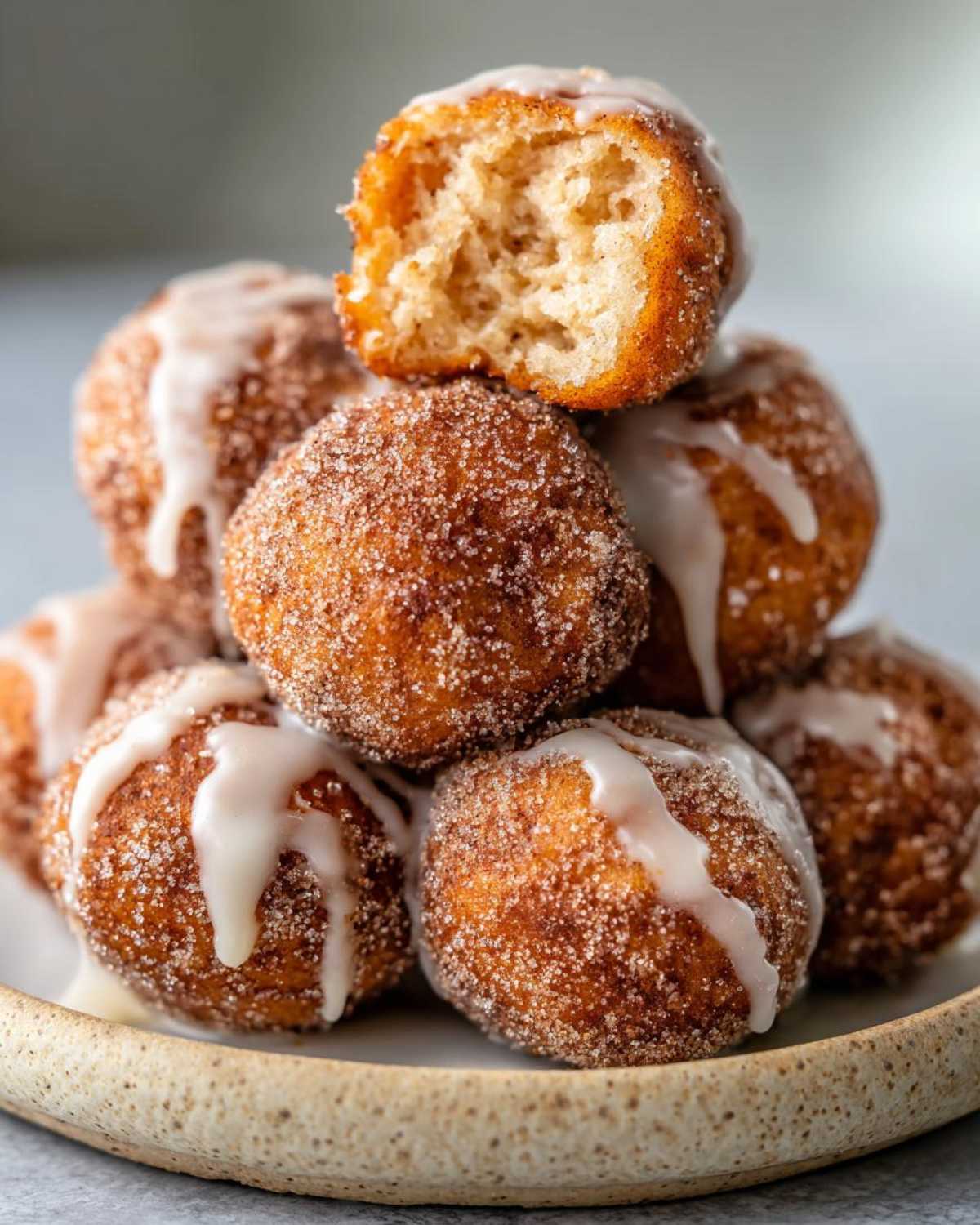 A stack of freshly made Apple Cider Donut Holes, coated in cinnamon sugar and drizzled with white glaze.