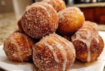 A close-up of a pile of freshly made Apple Cider Donut Holes, coated in cinnamon sugar and drizzled with a sweet glaze.