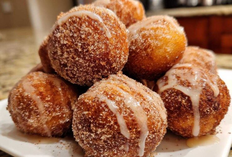 A close-up of a pile of freshly made Apple Cider Donut Holes, coated in cinnamon sugar and drizzled with a sweet glaze.