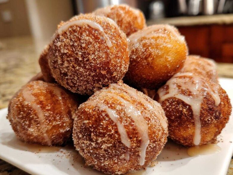 A close-up of a pile of freshly made Apple Cider Donut Holes, coated in cinnamon sugar and drizzled with a sweet glaze.