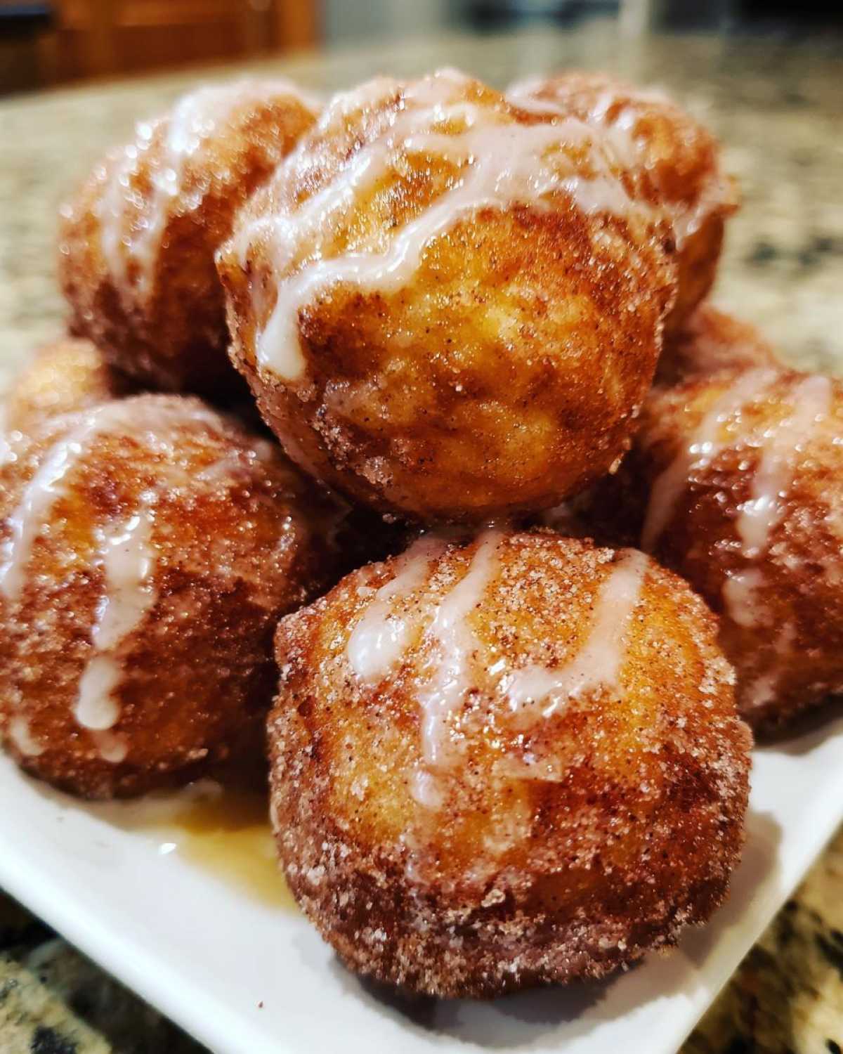A close-up of a pile of freshly made Apple Cider Donut Holes, coated in cinnamon sugar and drizzled with a sweet glaze.