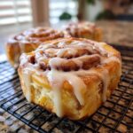 Close-up of freshly baked Apple Cinnamon Rolls drizzled with white glaze on a cooling rack.