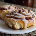 Two fluffy Apple Cinnamon Rolls generously drizzled with white icing on a white plate.