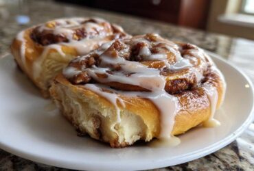 Two fluffy Apple Cinnamon Rolls generously drizzled with white icing on a white plate.
