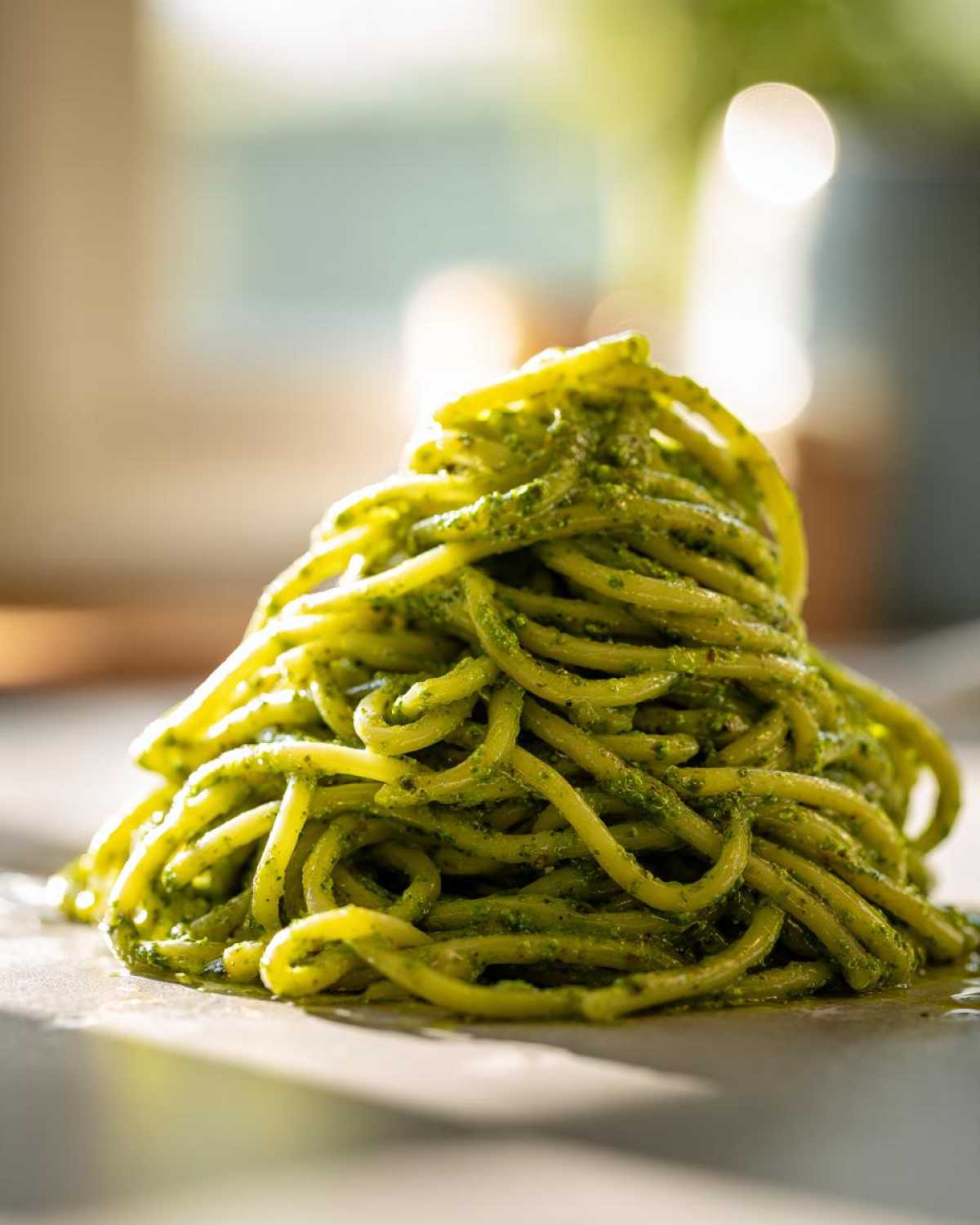 A close-up of a mound of spaghetti coated in vibrant green avocado pesto pasta sauce.