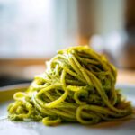 A close-up of a plate of spaghetti coated in vibrant green avocado pesto pasta.