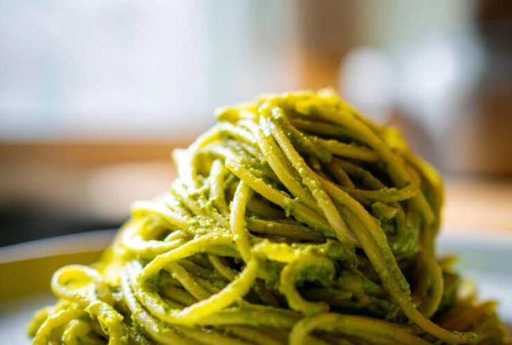 A close-up of a plate of spaghetti coated in vibrant green avocado pesto pasta.