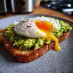 Close-up of delicious Avocado Toast with Poached Egg, showing the runny yolk dripping down.