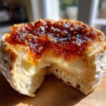 Close-up of a round of baked brie topped with glistening fig jam, with a slice removed to reveal the creamy melted cheese.