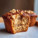A delicious banana walnut muffin with a bite taken out, showing the moist interior and visible walnuts.