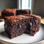 A close-up of a fudgy black bean brownie with visible chocolate chips on a white plate.