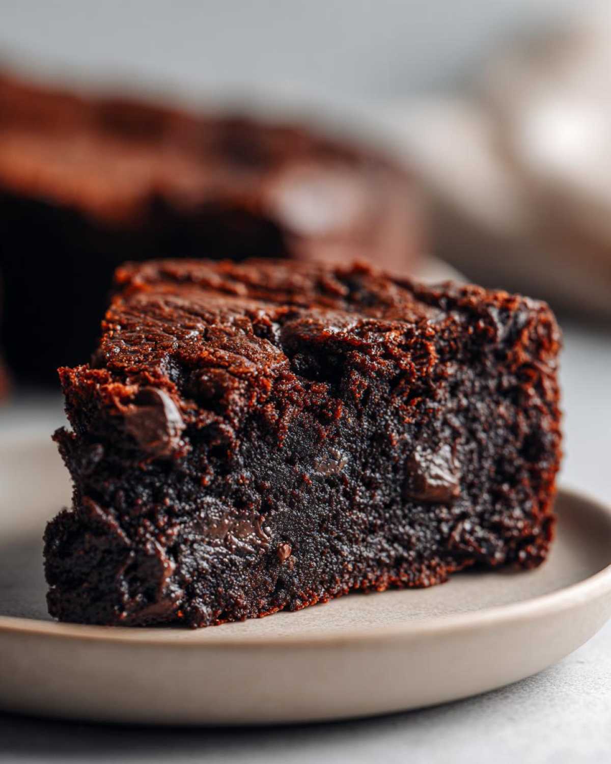 A close-up of a rich, fudgy slice of Black Bean Brownie on a plate, showing melted chocolate chips.