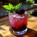 A refreshing Blackberry Basil Gin Smash cocktail in a glass, garnished with a fresh blackberry and basil leaves.