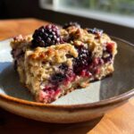 A close-up of a slice of Blackberry Maple Oatmeal Bake, topped with fresh blackberries.