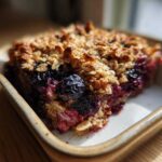 A close-up of a slice of Blackberry Maple Oatmeal Bake in a baking dish, showing the oatmeal topping and berry filling.