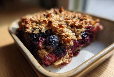 A close-up of a slice of Blackberry Maple Oatmeal Bake in a baking dish, showing the oatmeal topping and berry filling.