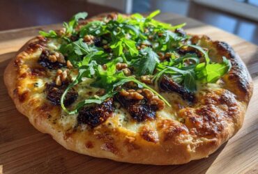 A delicious Blue Cheese & Fig Flatbread topped with fresh arugula and walnuts on a wooden board.