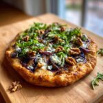 A delicious Blue Cheese & Fig Flatbread topped with walnuts, arugula, and red onion on a wooden board.