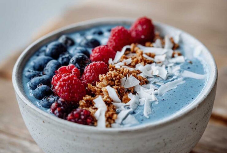 A close-up of a Blue Spirulina Smoothie Bowl topped with fresh blueberries, raspberries, granola, and shredded coconut.