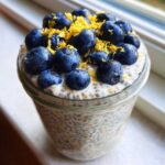 A close-up of Blueberry Lemon Chia Pudding topped with fresh blueberries and lemon zest in a glass jar.