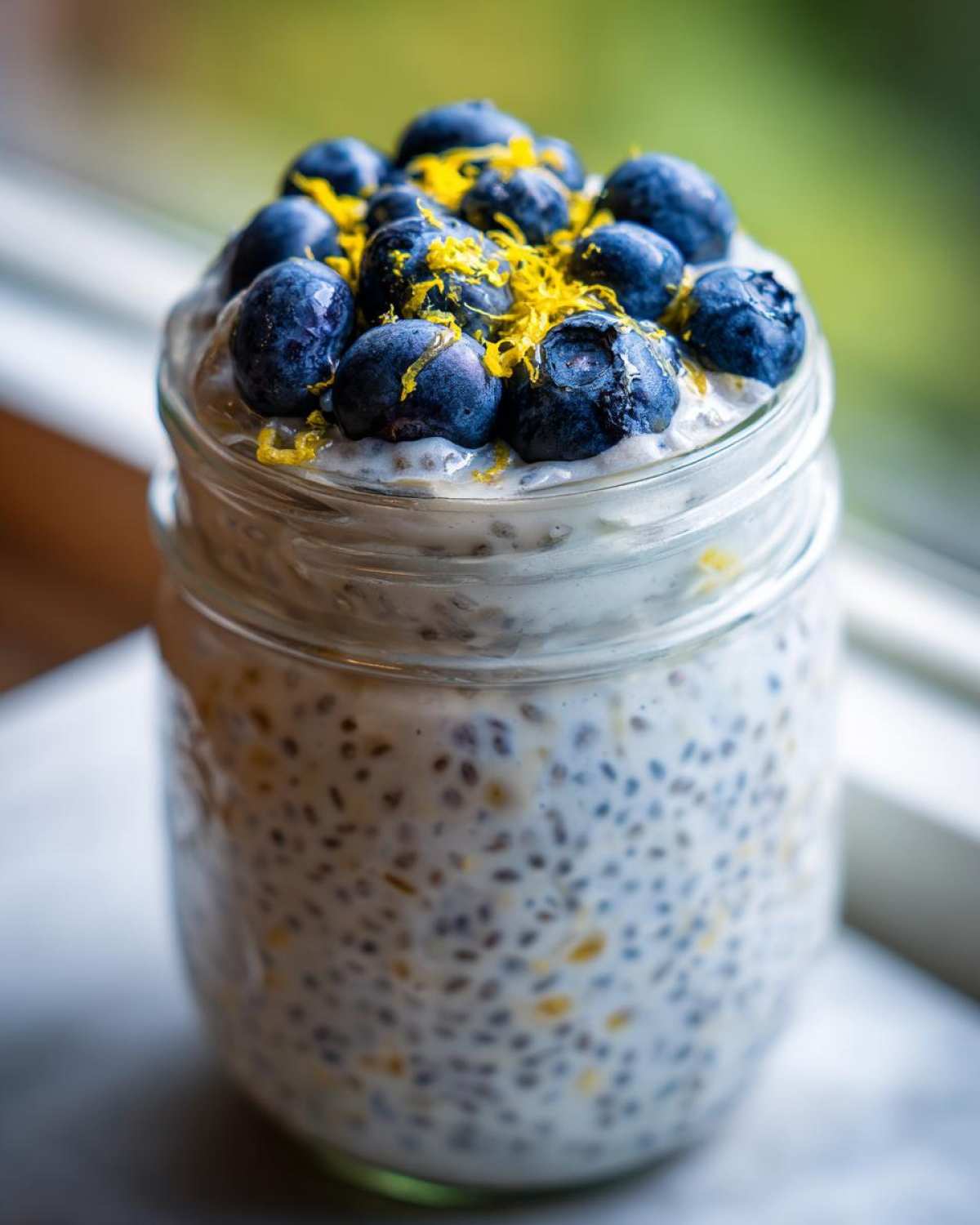 A glass jar filled with Blueberry Lemon Chia Pudding, topped with fresh blueberries and lemon zest.
