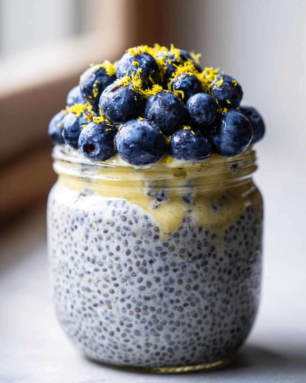 A close-up of Blueberry Lemon Chia Pudding in a glass jar, topped with fresh blueberries and lemon zest.