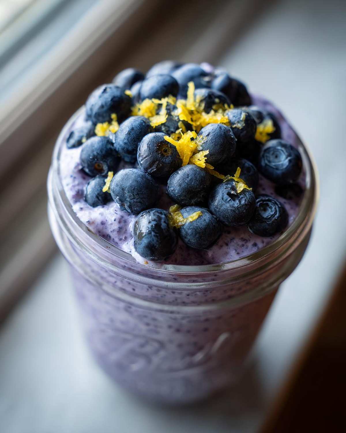 A close-up of Blueberry Lemon Chia Pudding in a jar, generously topped with fresh blueberries and lemon zest.
