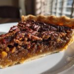 A close-up of a slice of delicious Brown Butter Bourbon Pecan Pie on a white plate.