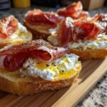 Close-up of delicious Burrata & Prosciutto Crostini topped with olive oil and herbs on a wooden board.