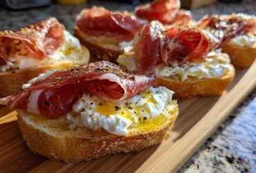 Close-up of delicious Burrata & Prosciutto Crostini topped with olive oil and herbs on a wooden board.
