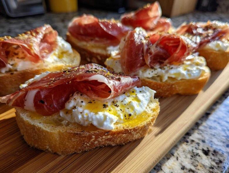 Close-up of delicious Burrata & Prosciutto Crostini topped with olive oil and herbs on a wooden board.