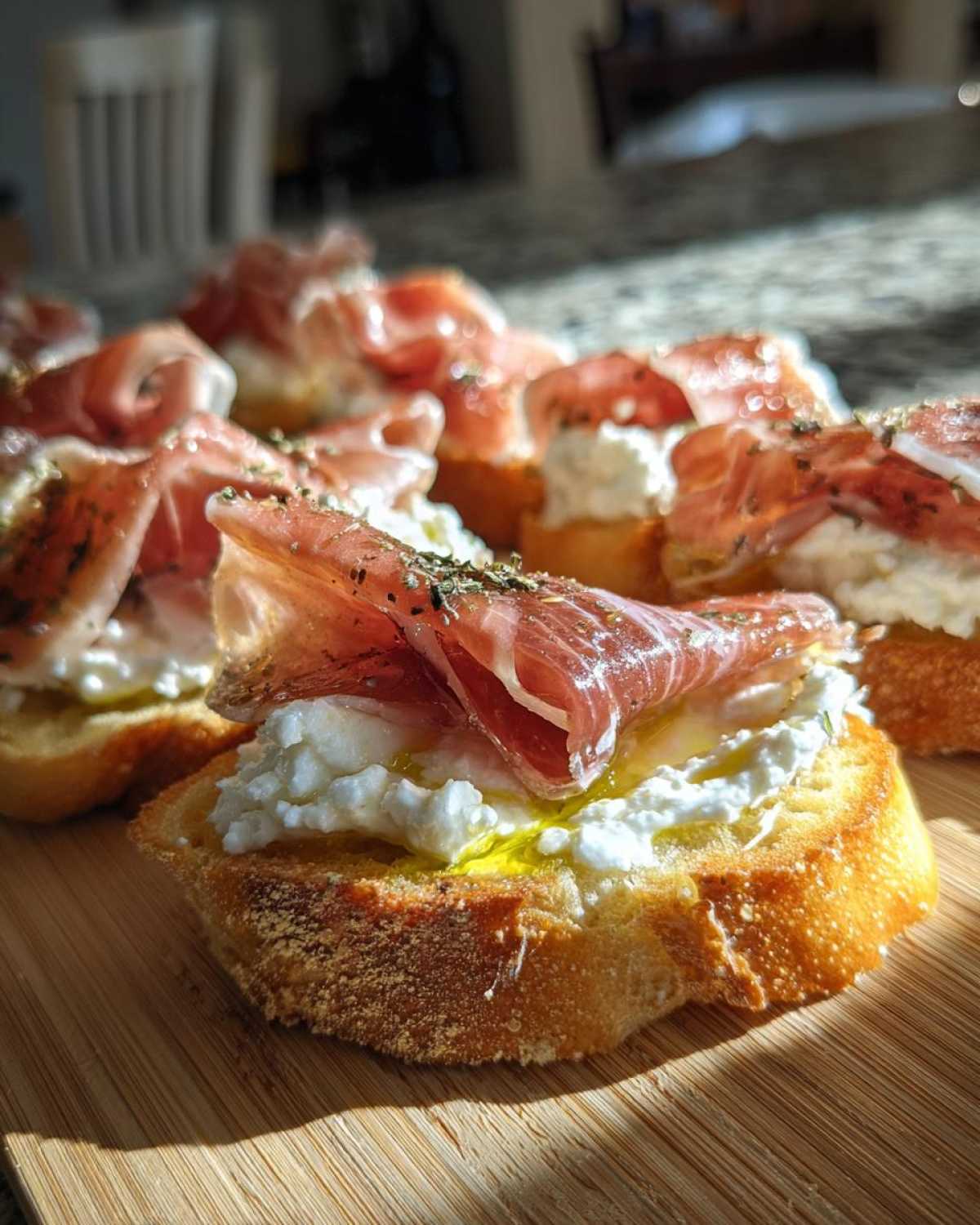Close-up of delicious Burrata & Prosciutto Crostini topped with olive oil and herbs on a wooden board.