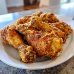 A close-up of a white plate filled with golden-brown Cajun Air Fryer Drumsticks, seasoned with spices and herbs.