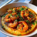 A close-up of a bowl of creamy grits topped with flavorful Cajun shrimp and fresh parsley.
