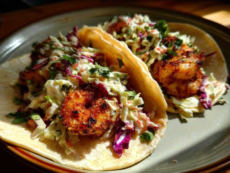Two delicious Cajun Shrimp Tacos filled with seasoned shrimp and a fresh, creamy coleslaw, garnished with cilantro.