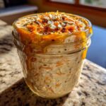Close-up of delicious Carrot Cake Overnight Oats in a jar, topped with shredded carrots, seeds, and drizzled with honey.