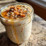A close-up of Carrot Cake Overnight Oats in a mason jar, topped with chopped nuts and drizzled with honey.