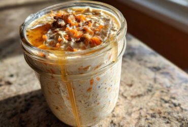 A close-up of Carrot Cake Overnight Oats in a mason jar, topped with chopped nuts and drizzled with honey.