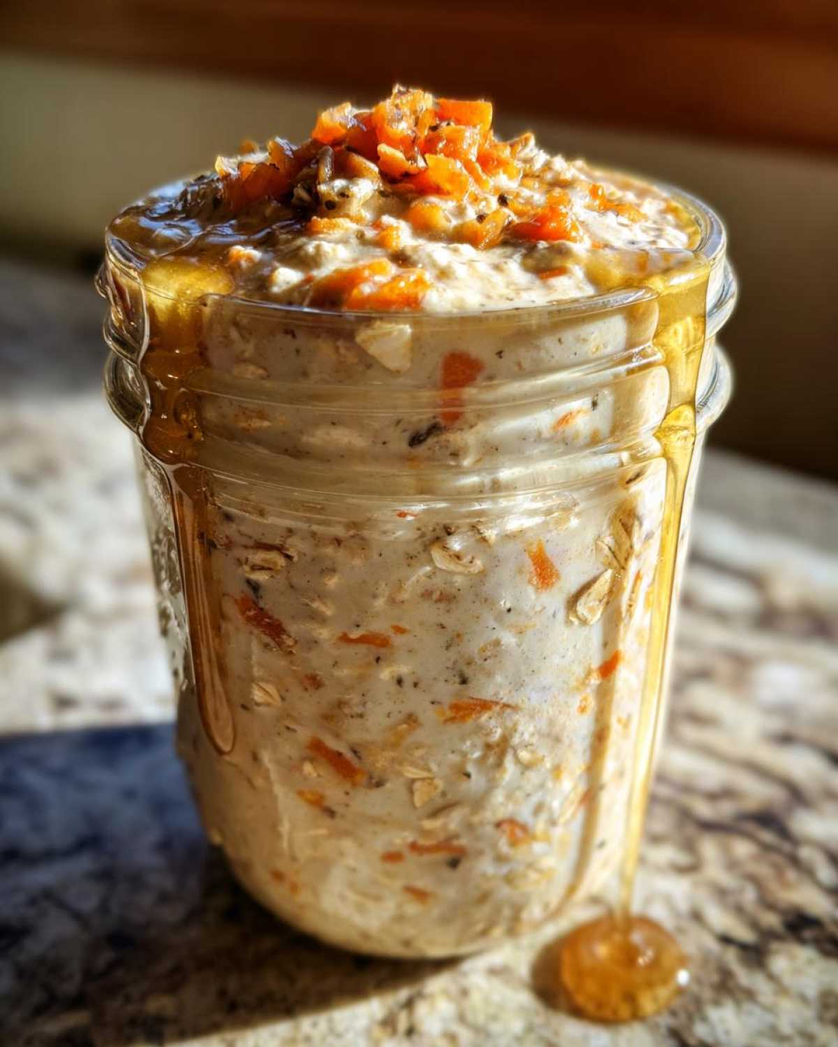 Close-up of Carrot Cake Overnight Oats in a glass jar, topped with shredded carrots and drizzled with honey.