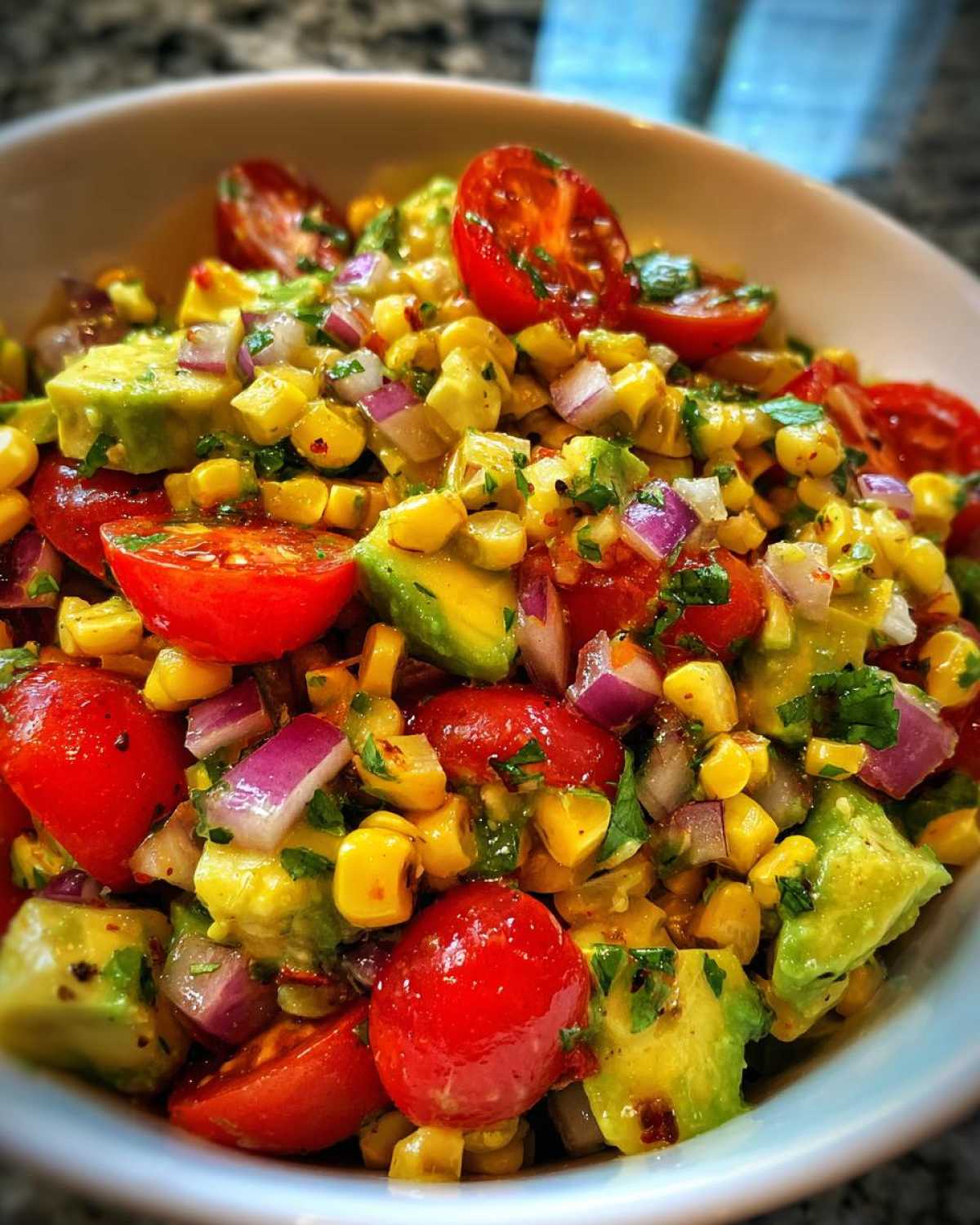 A vibrant close-up of Charred Corn & Avocado Salsa, featuring corn, avocado, cherry tomatoes, and red onion.