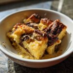 A close-up of a white bowl filled with moist Chocolate Babka Bread Pudding, showing swirls of chocolate and golden-brown baked bread.